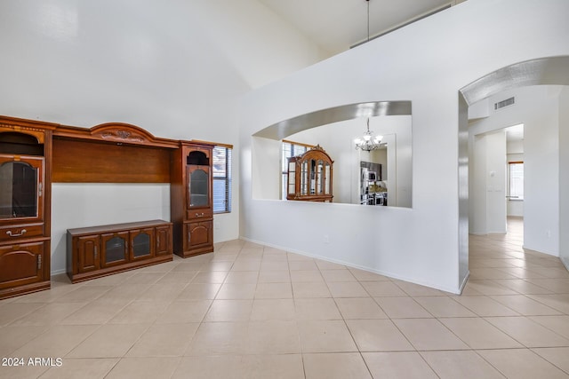 unfurnished living room with a high ceiling, a notable chandelier, and light tile patterned flooring