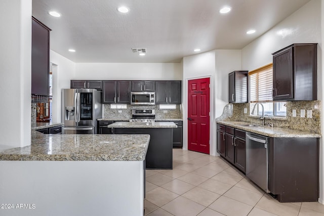 kitchen featuring sink, light stone counters, a kitchen island, and appliances with stainless steel finishes