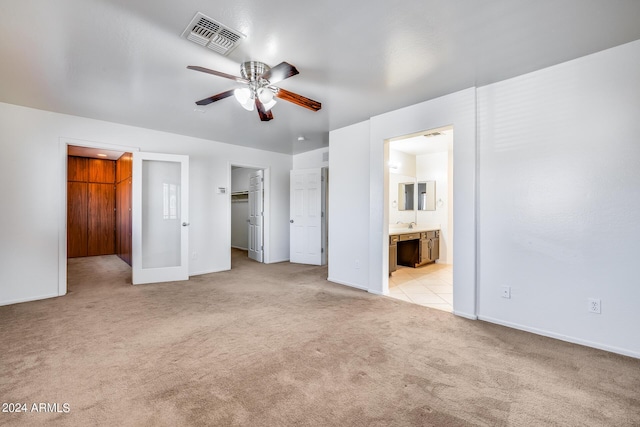 unfurnished bedroom featuring a spacious closet, ensuite bath, a closet, light colored carpet, and ceiling fan