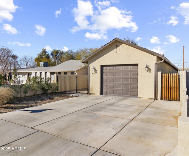 view of front facade featuring driveway, a garage, a gate, fence, and stucco siding