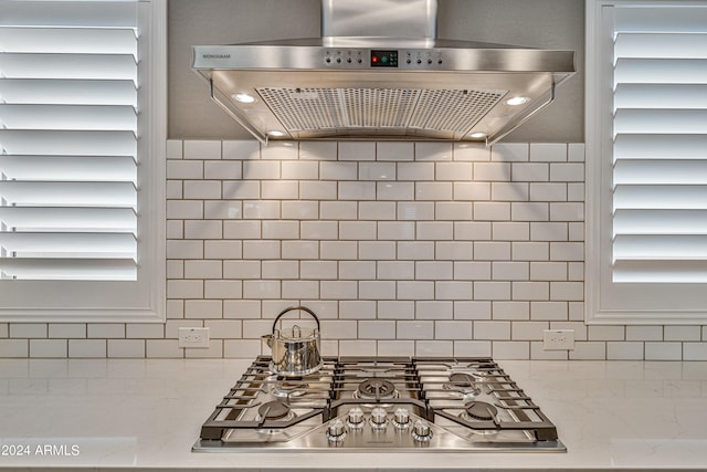 kitchen with light stone countertops, ventilation hood, stainless steel gas cooktop, and tasteful backsplash