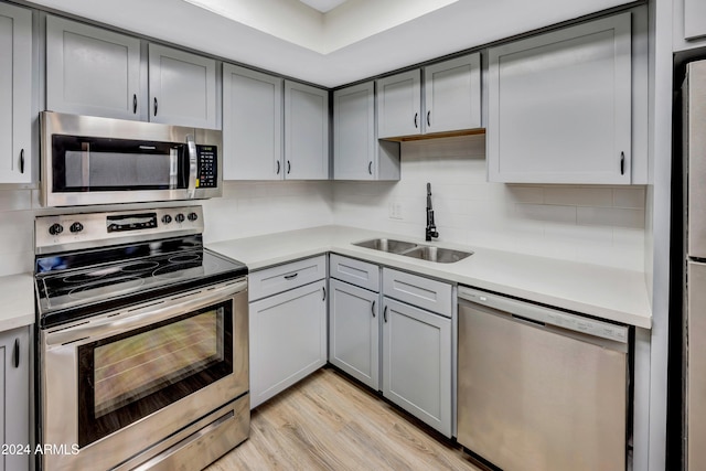 kitchen featuring tasteful backsplash, appliances with stainless steel finishes, light wood-type flooring, gray cabinets, and sink