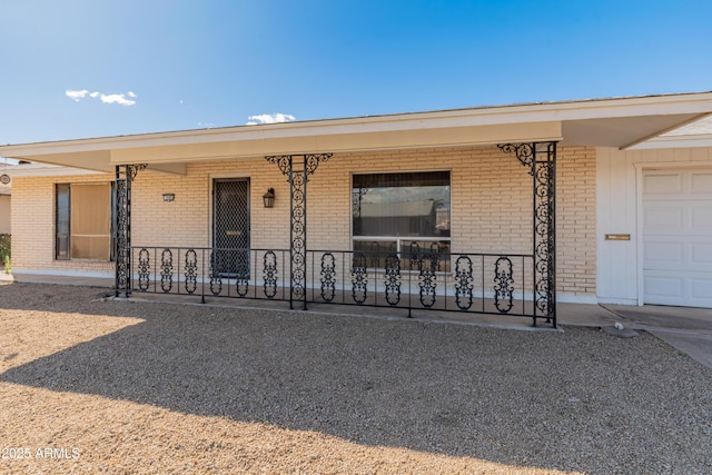 view of exterior entry with a garage, covered porch, and brick siding