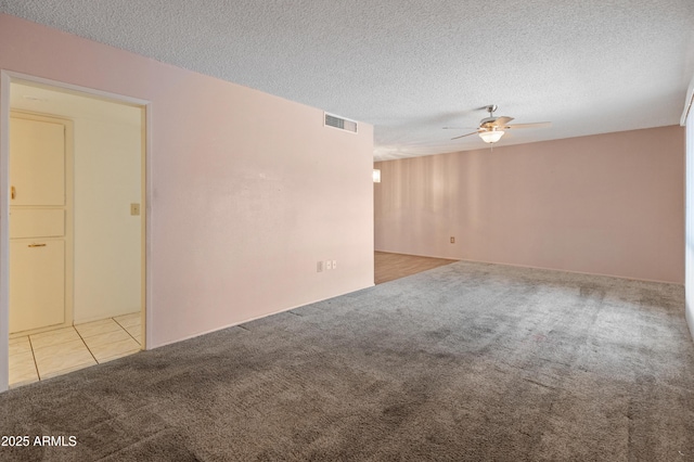 carpeted spare room featuring tile patterned flooring, visible vents, ceiling fan, and a textured ceiling