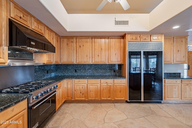 kitchen featuring under cabinet range hood, black refrigerator, visible vents, high end stainless steel range oven, and decorative backsplash