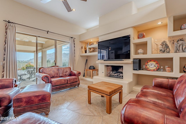 living room with built in shelves, a fireplace with raised hearth, a ceiling fan, and recessed lighting