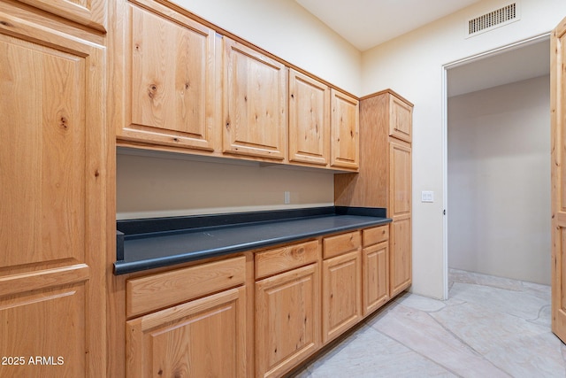 kitchen with light brown cabinetry, dark countertops, and visible vents