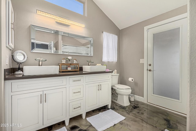 bathroom with lofted ceiling, double vanity, a sink, and toilet