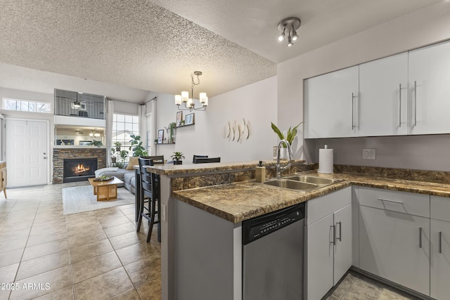 kitchen featuring a sink, a peninsula, stainless steel dishwasher, open floor plan, and dark countertops