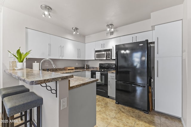 kitchen featuring visible vents, a peninsula, a breakfast bar, white cabinetry, and black appliances