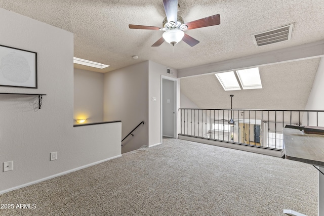 unfurnished room with carpet flooring, a textured ceiling, ceiling fan, visible vents, and lofted ceiling with skylight