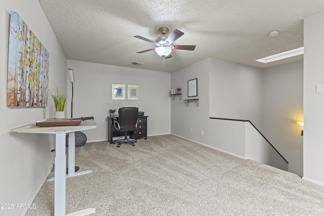 carpeted office space featuring a textured ceiling, visible vents, a skylight, baseboards, and ceiling fan
