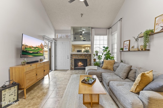 living room featuring a textured ceiling, high vaulted ceiling, ceiling fan, a stone fireplace, and light tile patterned floors