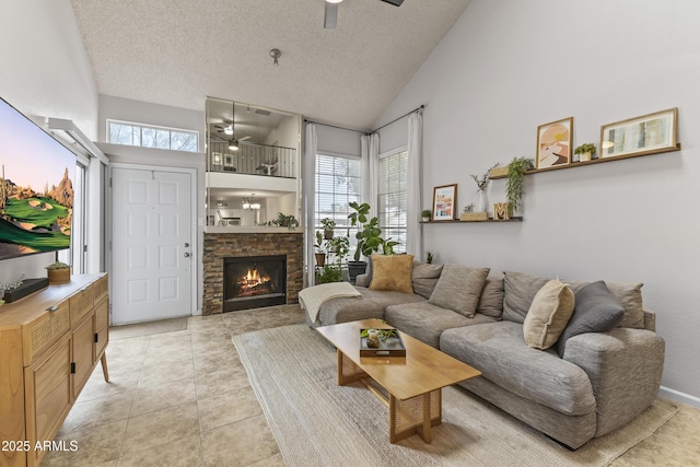 living room featuring high vaulted ceiling, a lit fireplace, a textured ceiling, light tile patterned flooring, and a ceiling fan