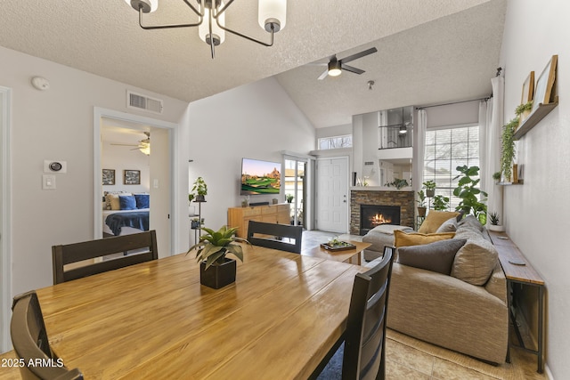 dining space with lofted ceiling, a fireplace, visible vents, and a ceiling fan