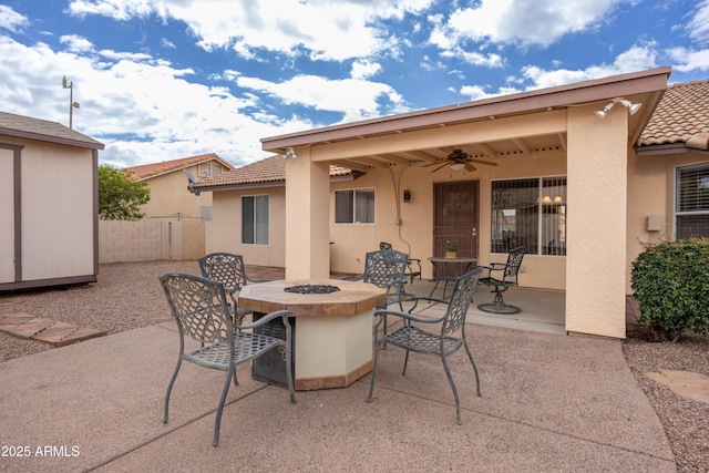 view of patio / terrace with fence, ceiling fan, outdoor dining space, a fire pit, and an outdoor structure