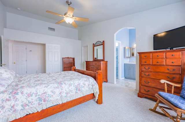 carpeted bedroom featuring arched walkways, ceiling fan, and ensuite bathroom
