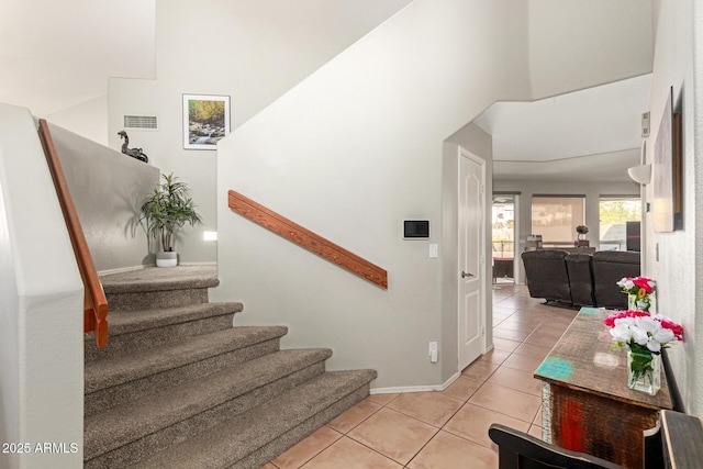 stairs with a towering ceiling, baseboards, visible vents, and tile patterned floors