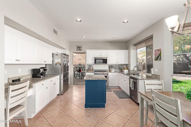 kitchen with white cabinets, a kitchen island, appliances with stainless steel finishes, light stone counters, and a sink