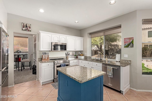 kitchen with light tile patterned floors, stainless steel appliances, a sink, white cabinetry, and light stone countertops