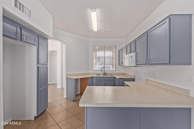 kitchen featuring gray cabinets, kitchen peninsula, light tile patterned flooring, and sink