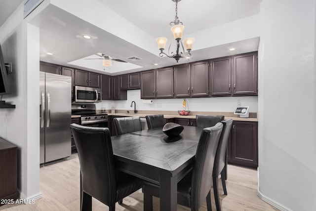 dining space with light hardwood / wood-style floors, sink, a raised ceiling, and ceiling fan with notable chandelier