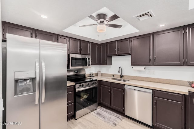 kitchen with light hardwood / wood-style floors, sink, a tray ceiling, and stainless steel appliances