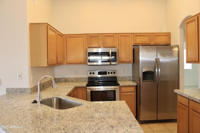 kitchen with appliances with stainless steel finishes, light stone countertops, sink, and light tile patterned floors