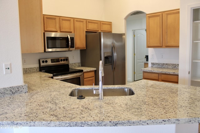 kitchen with kitchen peninsula, stainless steel appliances, light stone countertops, and sink