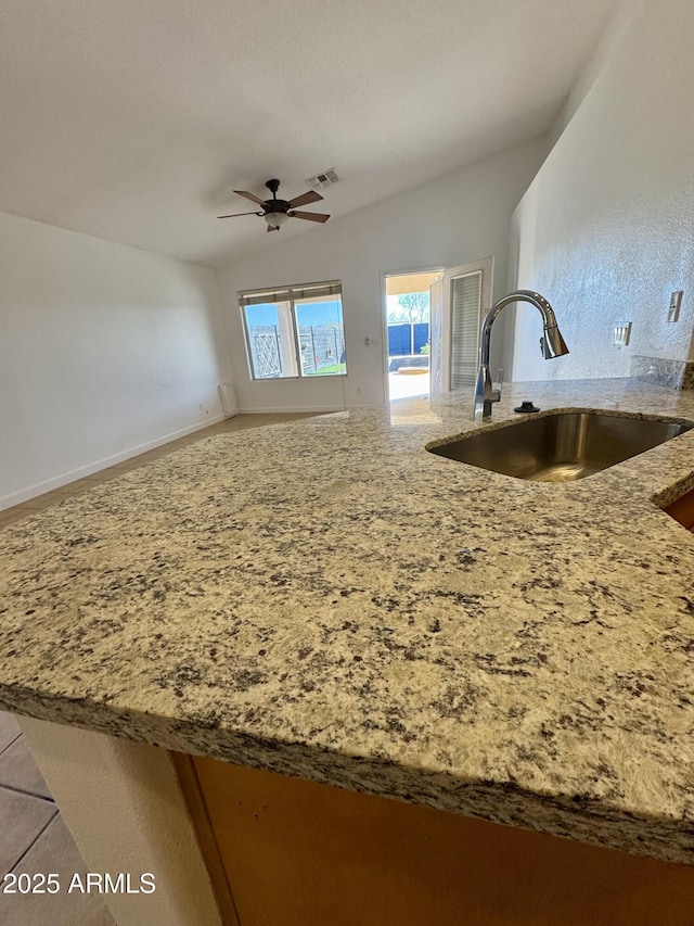 kitchen featuring sink, ceiling fan, vaulted ceiling, and light stone counters