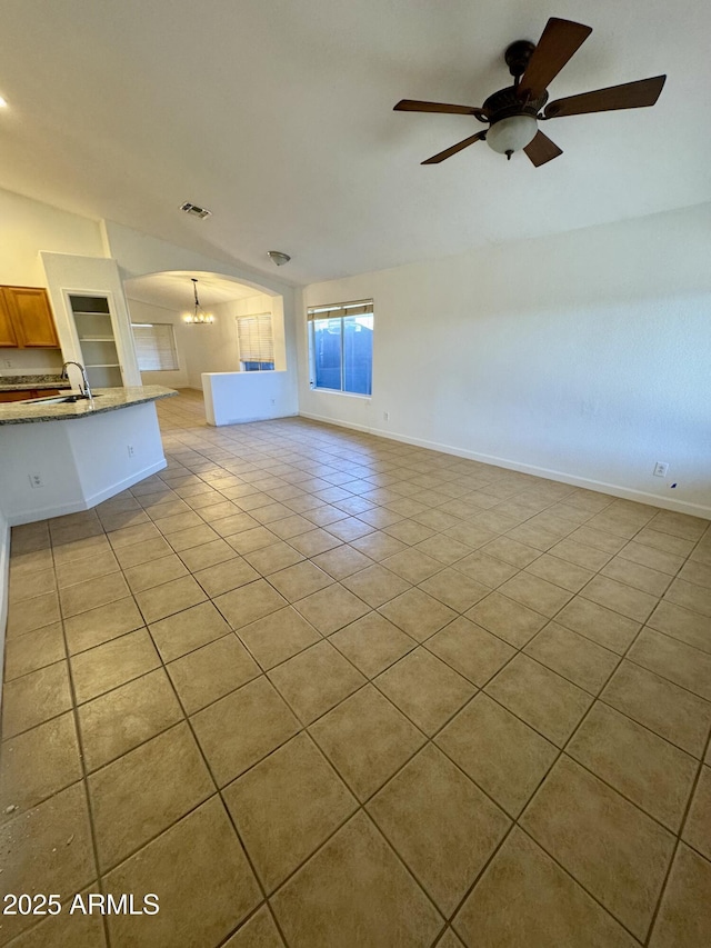 unfurnished living room featuring ceiling fan with notable chandelier, vaulted ceiling, sink, and light tile patterned floors