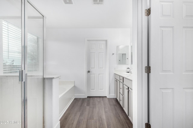 bathroom featuring wood finished floors, a shower stall, baseboards, a bath, and vanity