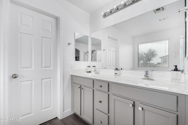 bathroom with a sink, wood finished floors, visible vents, and double vanity