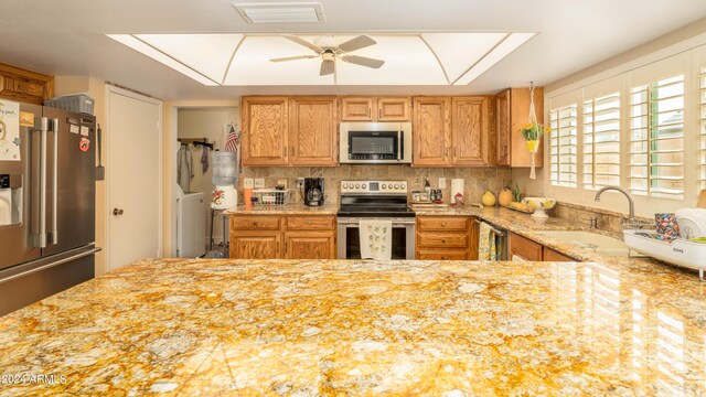 kitchen featuring appliances with stainless steel finishes, tasteful backsplash, sink, ceiling fan, and light stone counters