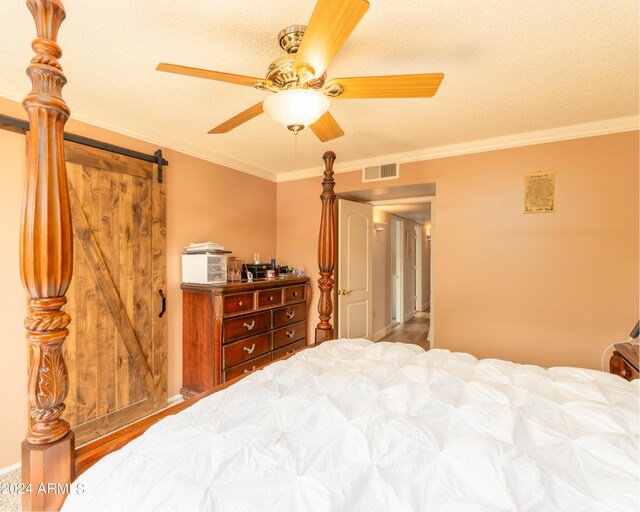 bedroom with a barn door, ceiling fan, crown molding, and a textured ceiling