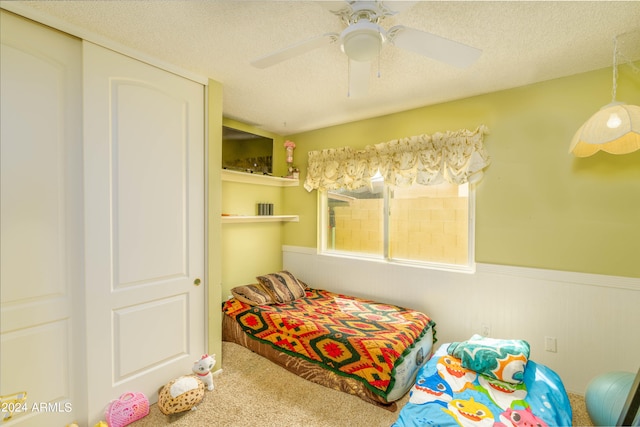 carpeted bedroom with a textured ceiling, ceiling fan, and a closet