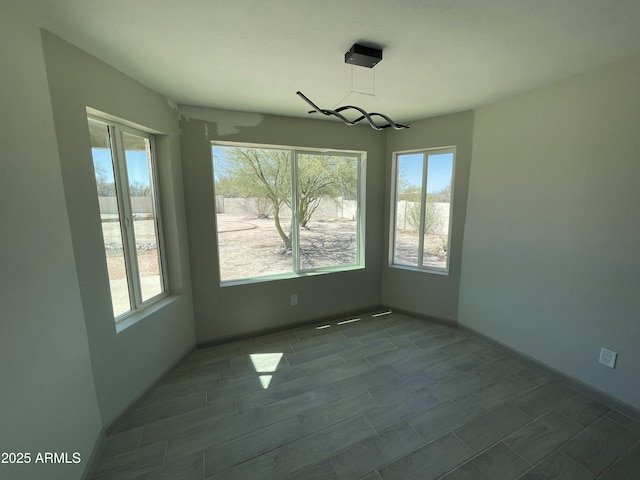 unfurnished dining area featuring an inviting chandelier, baseboards, and a healthy amount of sunlight