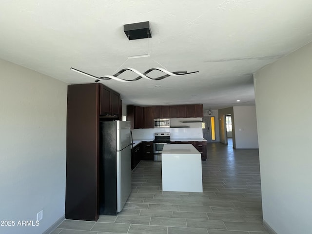 kitchen featuring a center island, open floor plan, baseboards, light countertops, and appliances with stainless steel finishes