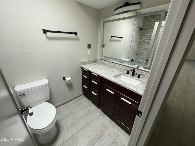 bathroom with vanity, toilet, baseboards, and tiled shower