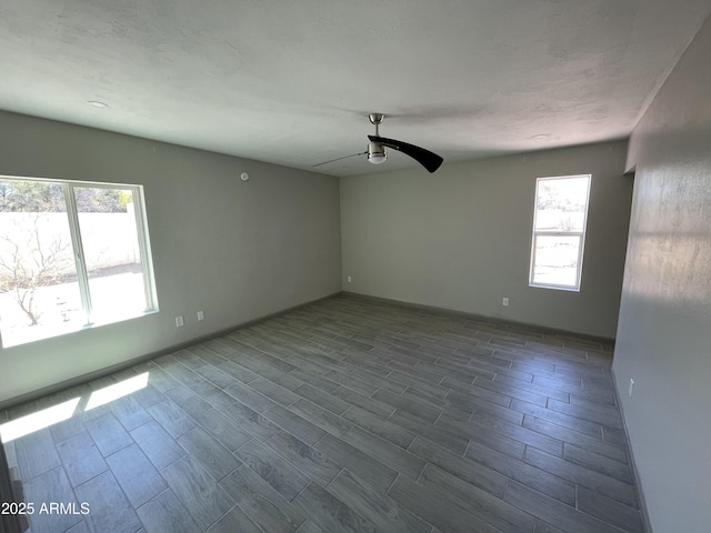 empty room with baseboards, dark wood finished floors, ceiling fan, and plenty of natural light
