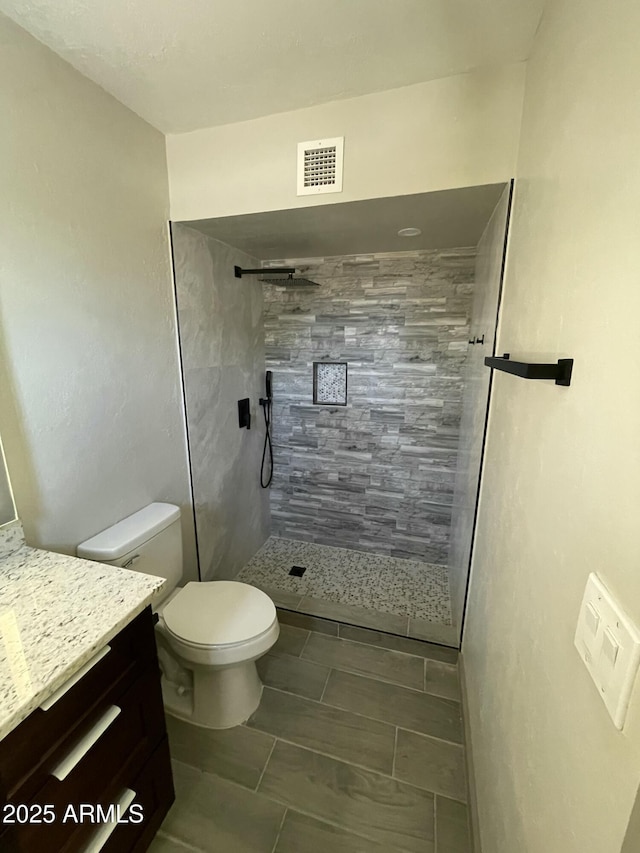 bathroom featuring toilet, vanity, visible vents, and a walk in shower