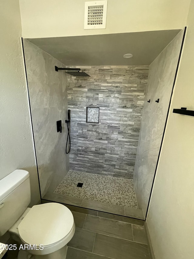bathroom featuring toilet, tile patterned flooring, a tile shower, and visible vents