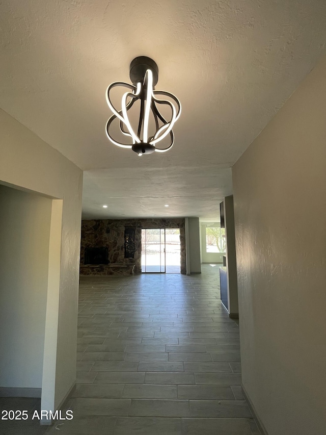 hallway with an inviting chandelier, a textured ceiling, baseboards, and wood finished floors