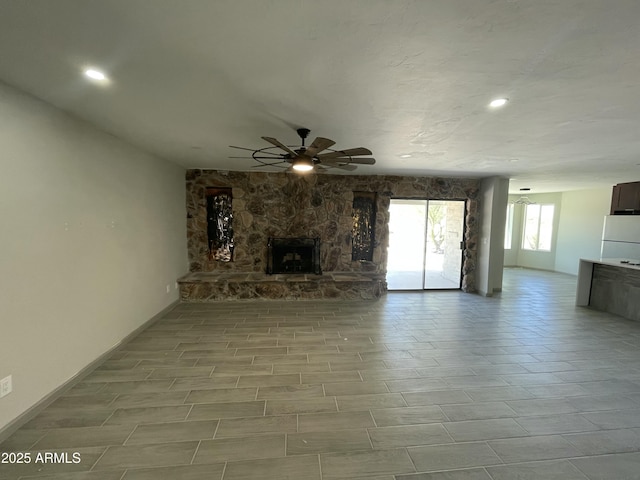 unfurnished living room featuring baseboards, a ceiling fan, a stone fireplace, and recessed lighting