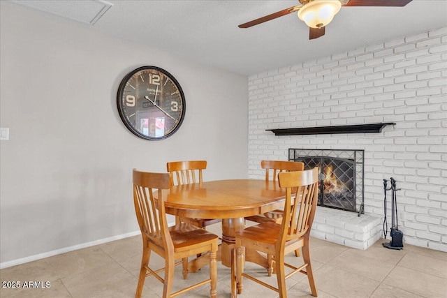 dining space featuring light tile patterned floors, baseboards, brick wall, ceiling fan, and a fireplace