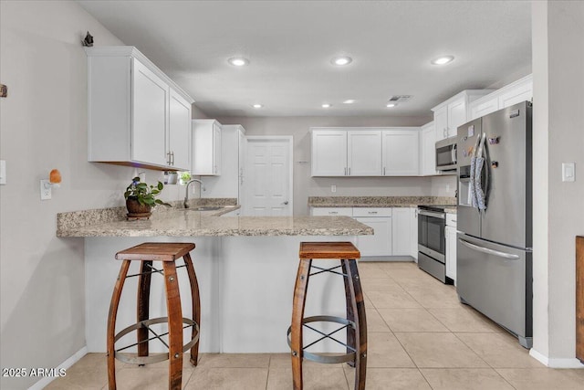 kitchen featuring stainless steel appliances, a sink, light stone countertops, a peninsula, and a kitchen bar