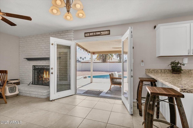 doorway to outside featuring a fireplace, a ceiling fan, and light tile patterned flooring