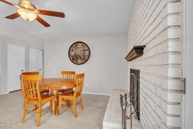 dining area with light tile patterned floors, attic access, baseboards, ceiling fan, and a brick fireplace