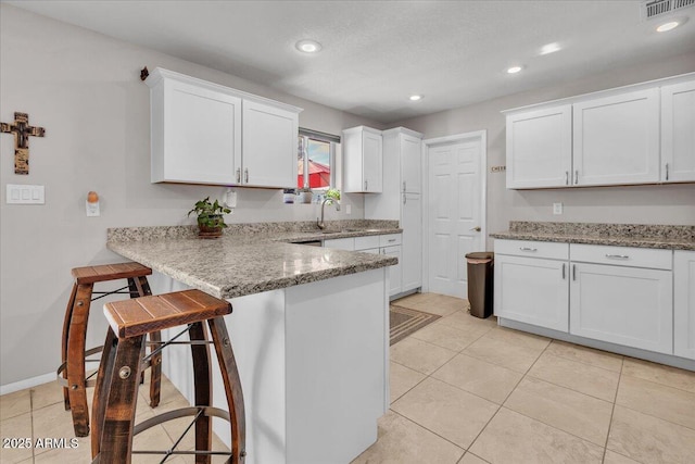 kitchen featuring a peninsula, white cabinetry, a kitchen breakfast bar, and light stone counters