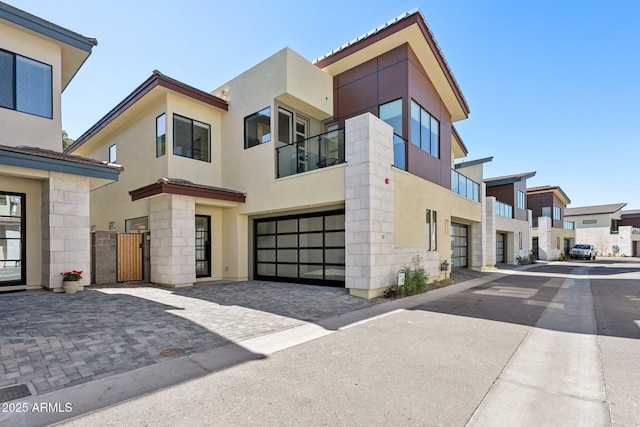 modern home with a garage, decorative driveway, stucco siding, a gate, and a residential view